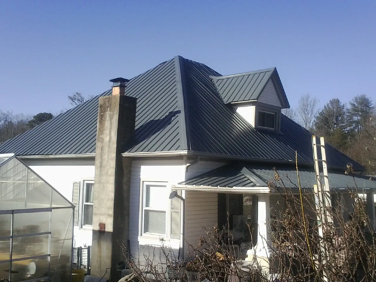 Dark blue standing seam metal roof on a white farmhouse with dormer — Slate & Tile Roof Repair by Roofing Brothers in Gaston